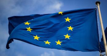 European Union flag on a flagpole blowing in the wind against blue sky