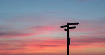 Sign with arrows point in different directions against a sunset