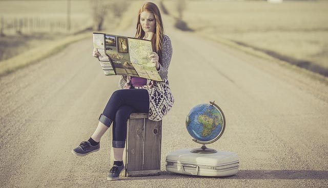 Girl sits on a suitcase reading a map with globe next to her