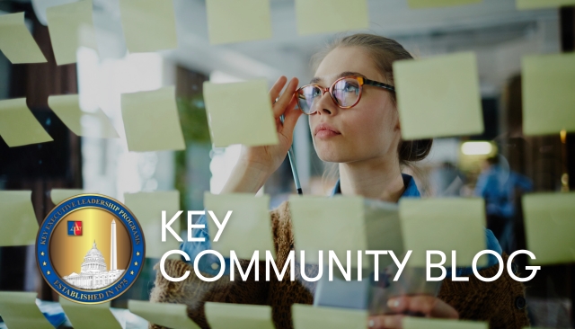 Key Community Blog with a woman standing in front of a clear board covered in post it notes as she prepares for a work project