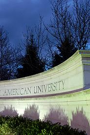 American University sign illuminated at night with lights against a dark sky