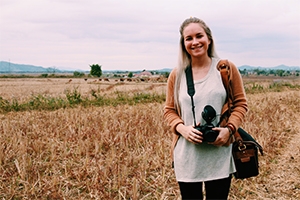 Erin McGoff standing in a field with a DSLR camera in Laos during her Alternative Break trip in the winter break of 2016-17.