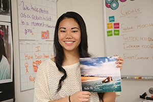 Chua, with long dark hair, holds a copy of the her new photo book. The cover features a sunny beach scene.