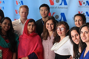 Malala Yousafzai in a red head scarf stands with a group of students, including Babu and Mammadova.