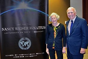 Nancy Weiser Ignatius and Paul Ignatius pose with the event banner for the Nancy Weiser Ignatius Lecture for the Environment.