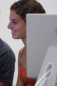 Smiling student seated by Mac computer looking at the screen