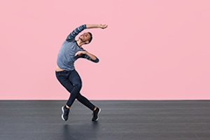 Male dancer on stage in front of pink background.