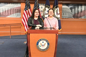 Tracy Hanqing and a friend post at a speaker's at the U.S. House of Representatives, flags on display close behind them.