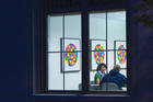 Students study in room with art on walls, photo shot from outside window into room