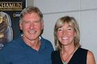 Harrison Ford stands with Maggie Stogner in front of a poster for the National Geographic King Tut exhibit. Ford Narrated Stogner's video for the exhibition.