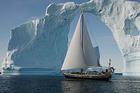 Photo of sail boat in the arctic sailing under an ice bridge.