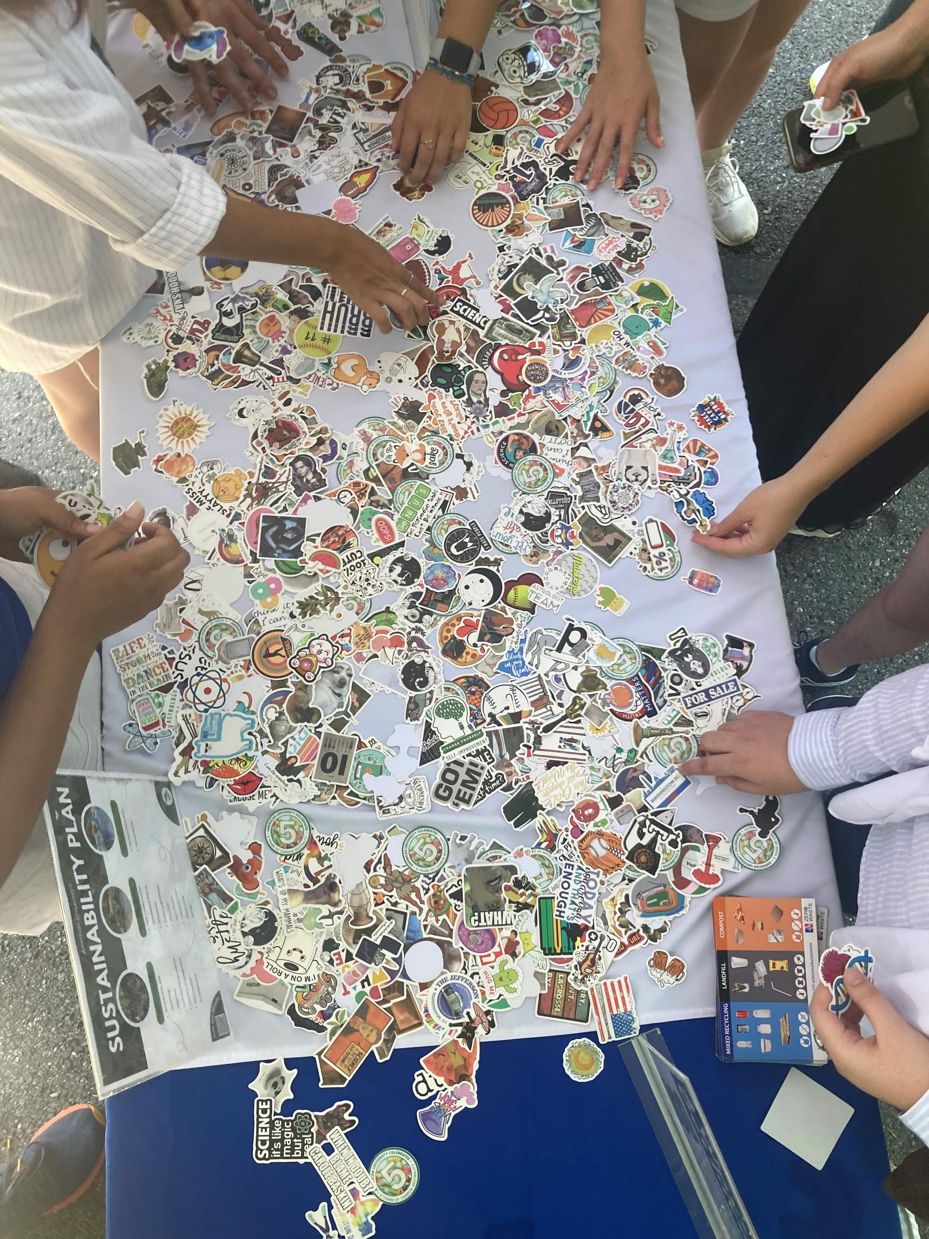 Several sets of hands reach for stickers spread out on a blue tablecloth.