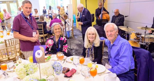 A table of four Golden Eagle alumni gather for a photo in front of a live band.