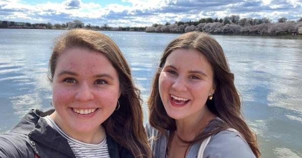 Emily (left) and Molly (right) Molloy pose near the Tidal Basin overlooking pink cherry blossoms.