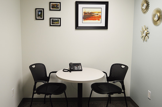 Two black chairs on either side of a round table. Framed pictures are on the wall above the table.