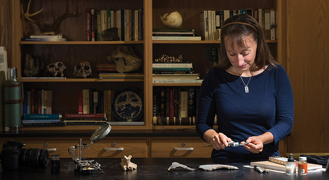 Becca Peixotto examines an artifact with a magnifying glass.