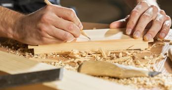 Hands holding board and pencil on woodworking bench