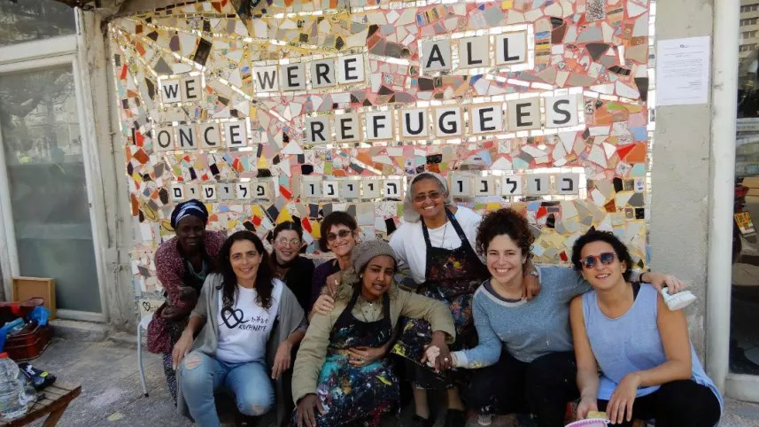 Women posed before "we were all once refugee" wall.