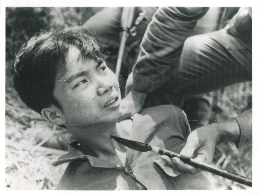 A man holds an arrow to a boy's neck. Eddie Adam, photographer.