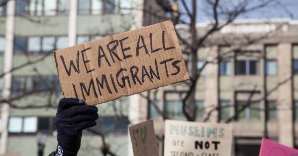 Gloved hand holds cardboard sign reading "We are all immigrants"