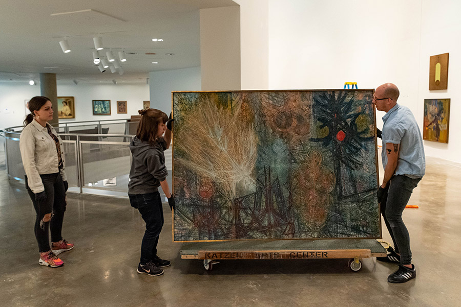 Three people move one of the pieces of art from a cart