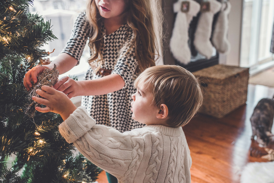 Two kids hang ornaments on a tree