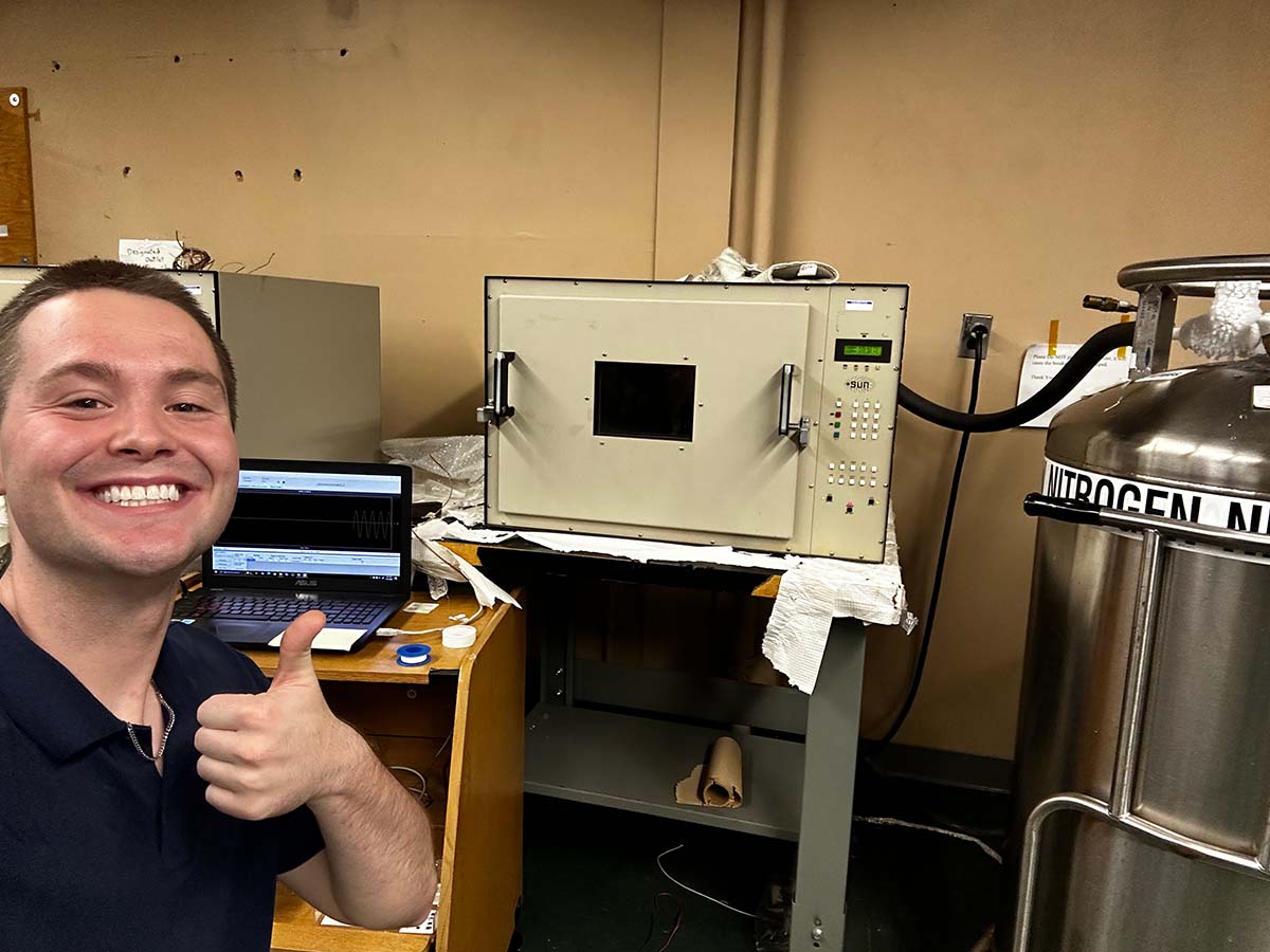  Isaac Salmon standing beside a temperature test chamber, which cycles materials between temperature extremes to measure how their performance changes. 