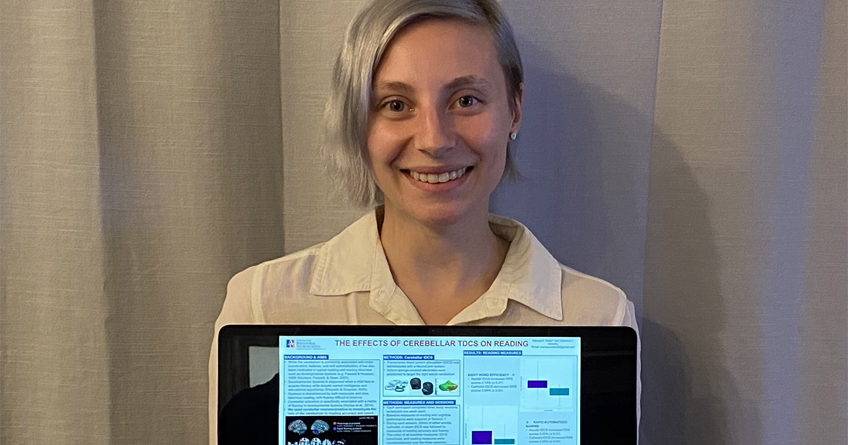 A student poses with a laptop that is displaying their research poster