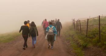 People on dirt road along barbed-wire fence.