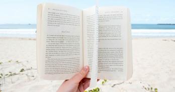 Hand holding an open book on the beach
