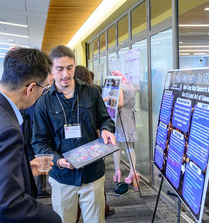 Student discussing poster and rap album with faculty.