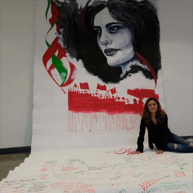 Phaedra Askarinam with artwork showing a Mahsa Amini's face in context of protests in Iran and human rights declarations.