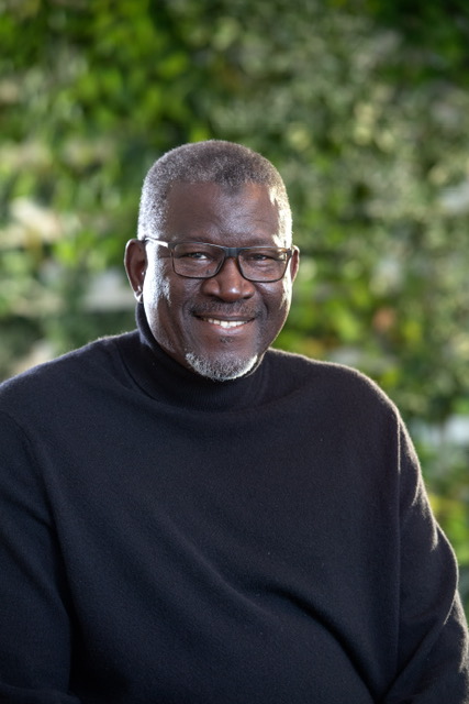 A black man in a black turtle neck and glasses smiles at the camera