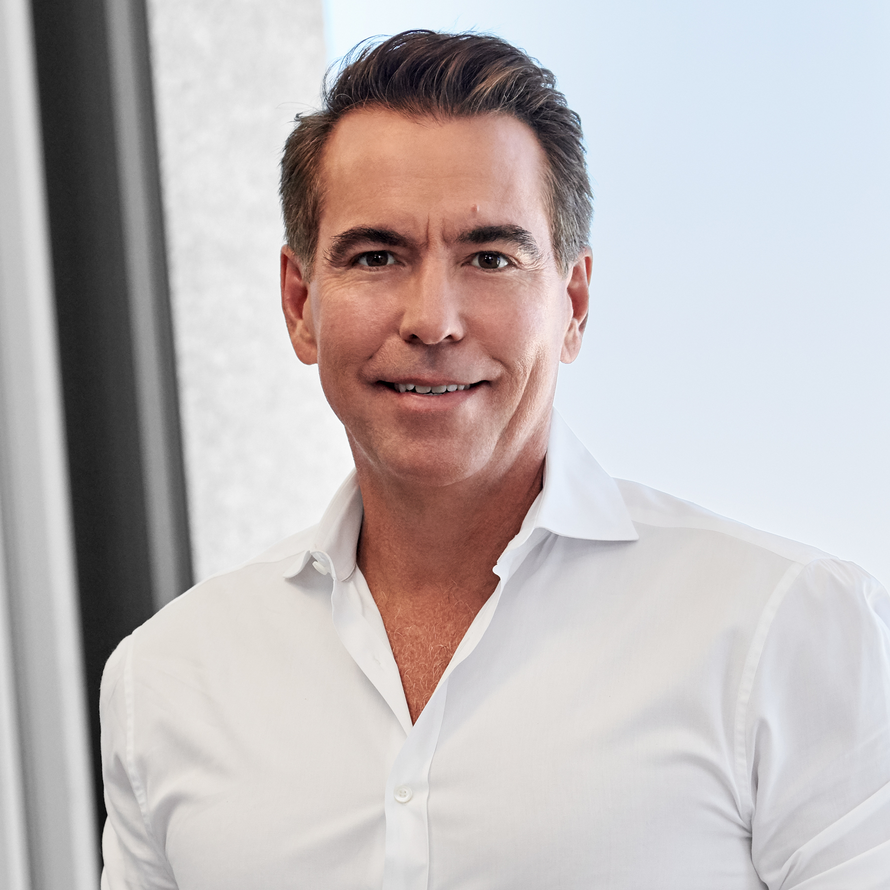 a man in a white button up with salt and pepper hair looks and smiles a the camera