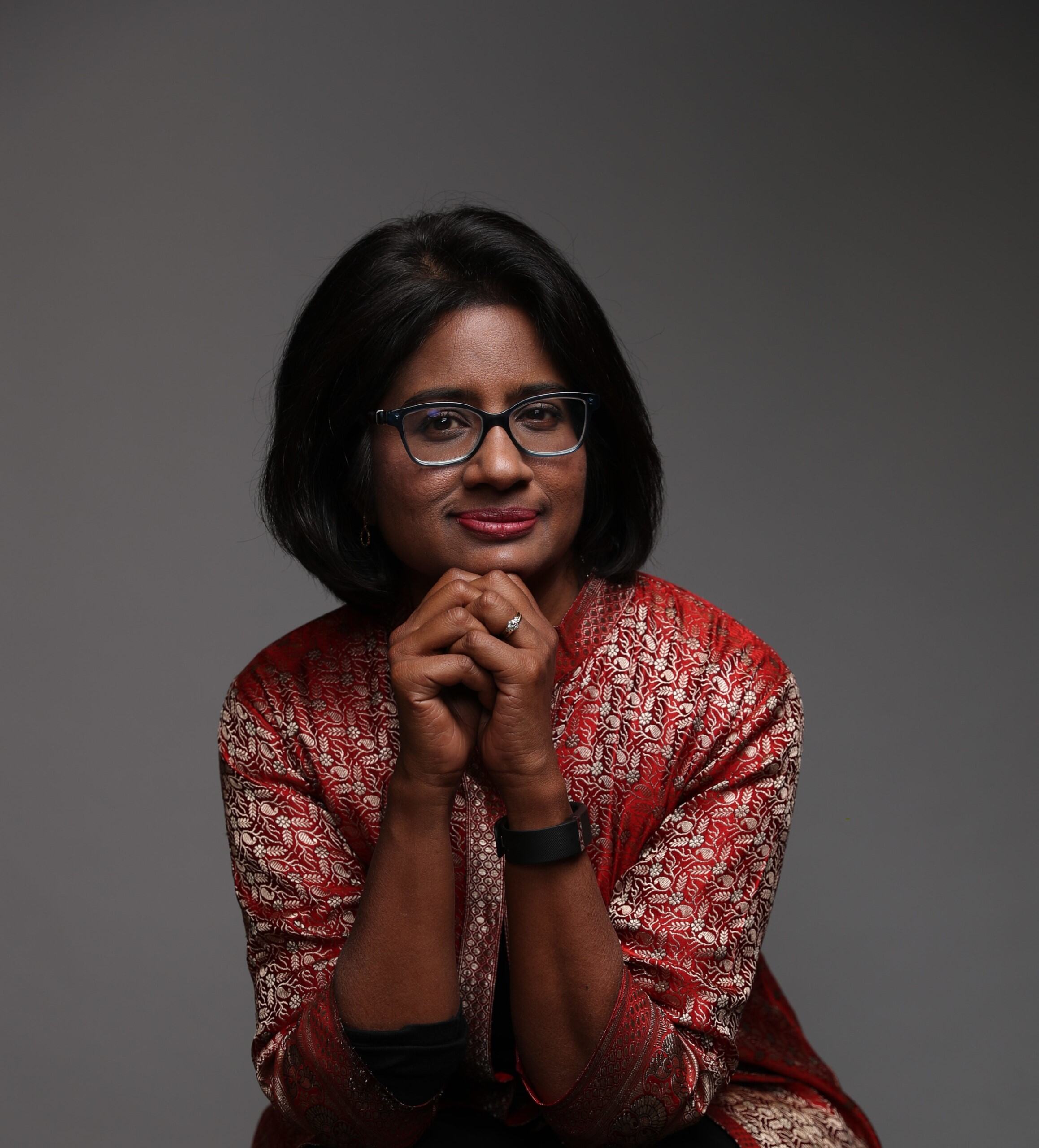 image of a young woman with glasses with her hands under her chin looking at the camera and smiling