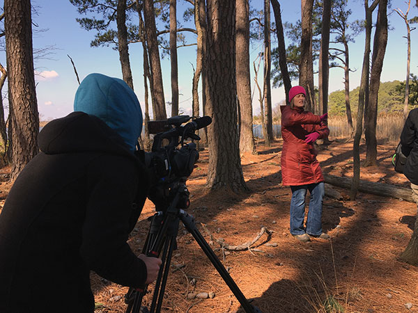 A filmmaker records a documentary presenter in a wooded area