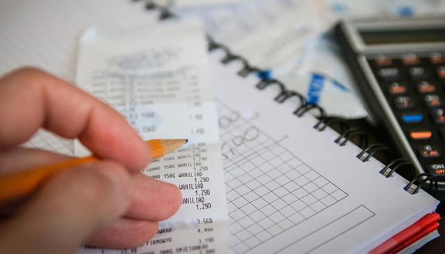 A hand with a pencil, with a receipt and a calculator in the background