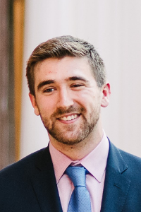 AU Student, Joseph, wearing a blue suit jacket , pink shirt, and light blue tie 