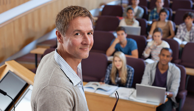 Male faculty at podium with classroom behind him