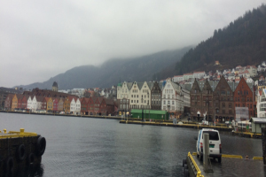 A body of water in Norway adjacent to homes and mountains with an overcast sky