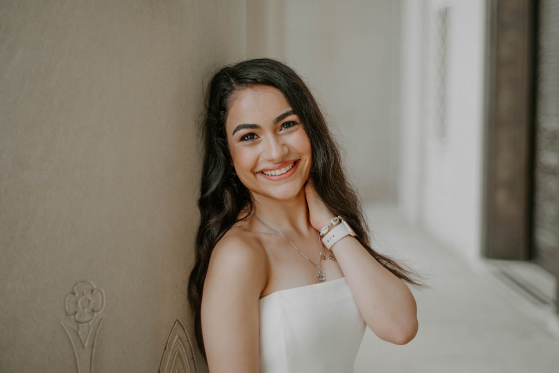 Rose wearing a white sleeveless shirt leaning against the wall while smiling at the camera