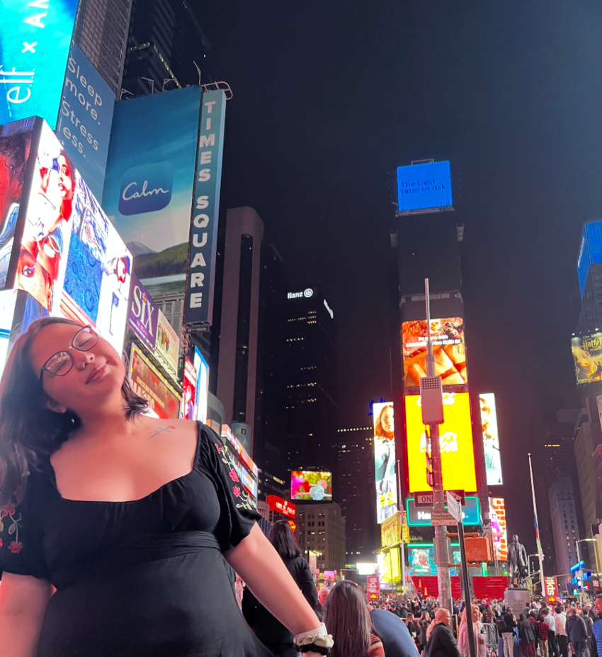 Maddy in a black dress standing in Times Square in New York City