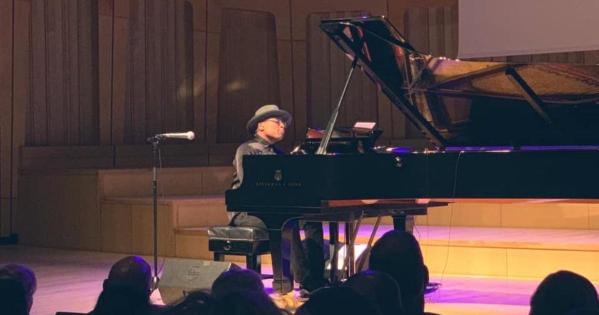 Alexis Ffrench, a black man, plays a grand piano on a stage