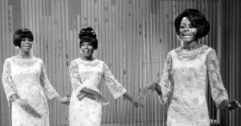 Three black women perform in light colored lace dresses