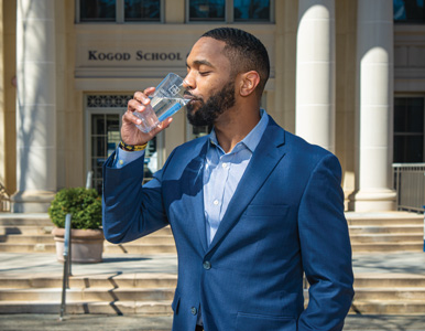 Korey Salter drinks from a water glass in front of the Kogod School of Business