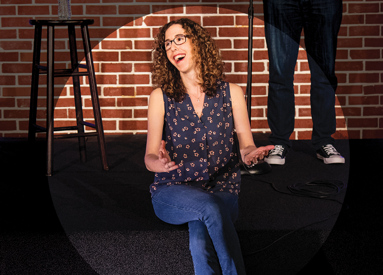 Allyson Jaffe sits and laughs on the DC Improv stage