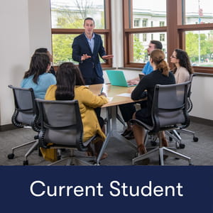 Current Student: professor teaching a group of graduate students sitting around a table