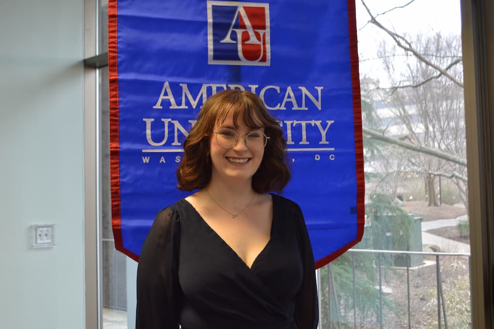 Madeleine Corrigan standing in front of AU banner