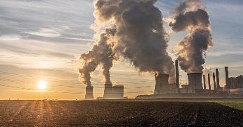 a coal plant with the sun setting over a field