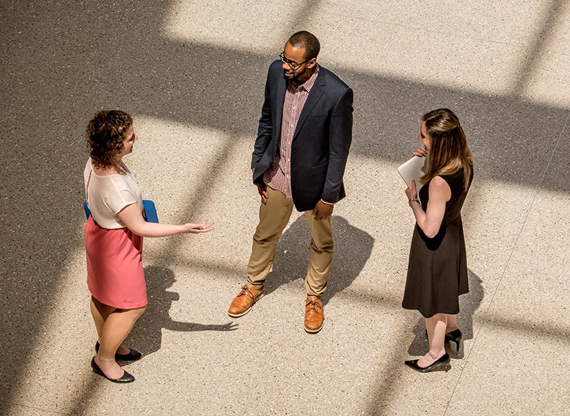 Three students talk to each other in the SIS atrium.